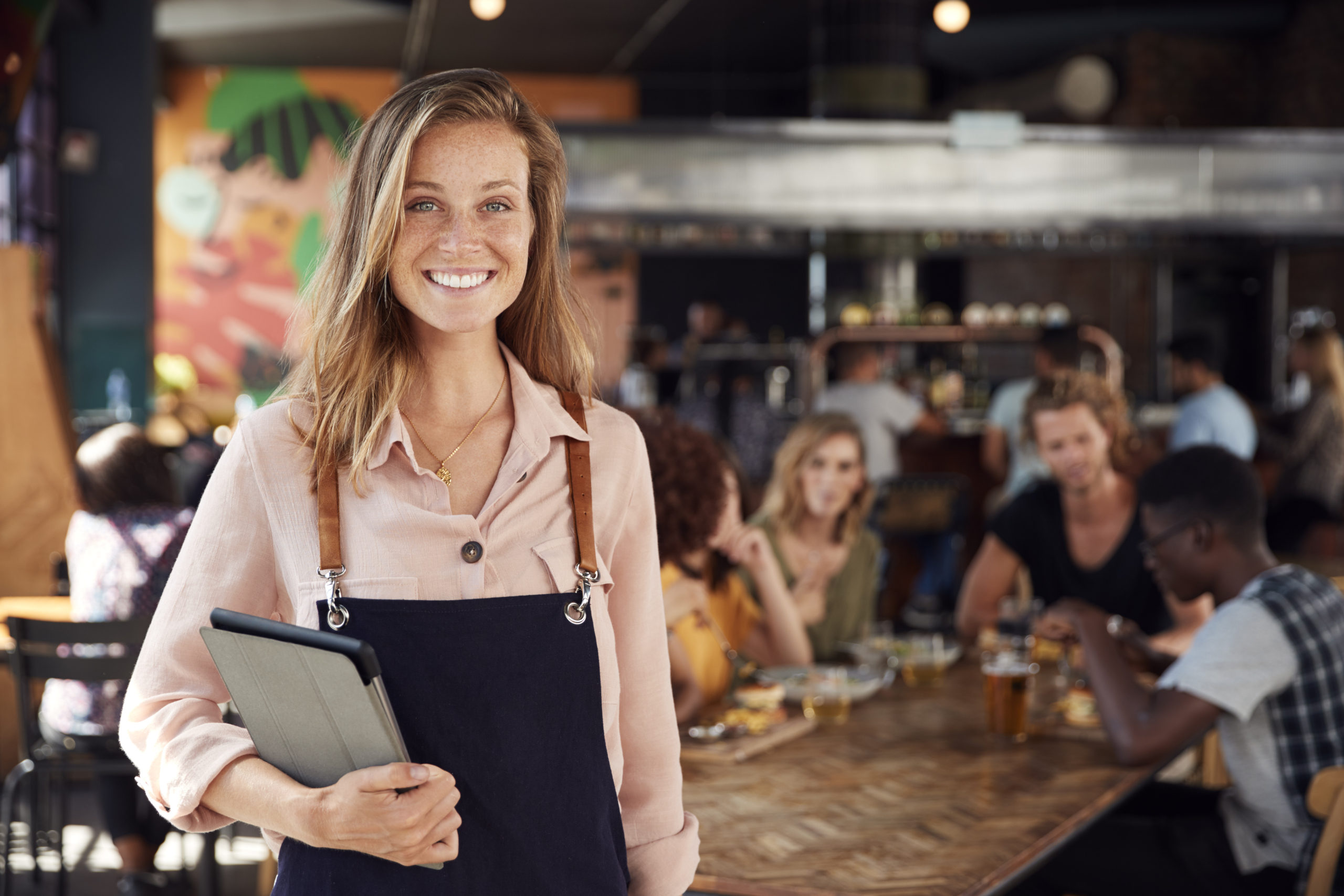 Portrait Of Waitress Holding Menus Serving In Busy Bar Restaurant